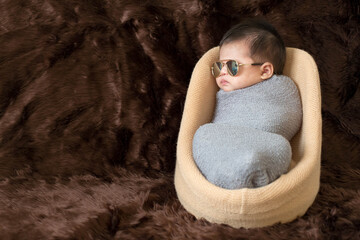 Cute Asian newborn baby wrap with grey blanket on brown fur background. Nice portrait of little child boy and glasses. sunglasses

