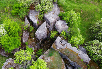 A view from a height on a stone rock ruins in a green field. Remains of an old fort of World War II