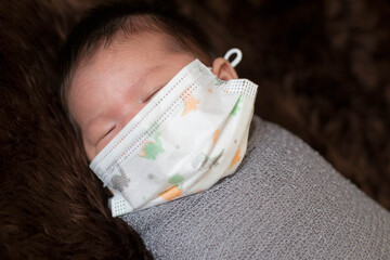 Cute Asian newborn baby wrap with grey blanket on brown fur background. Nice portrait of little child boy and face mask
