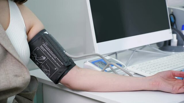 Woman patient undergoes procedure of pressure measuring with digital tonometer sitting at doctor table with monitor in hospital office closeup