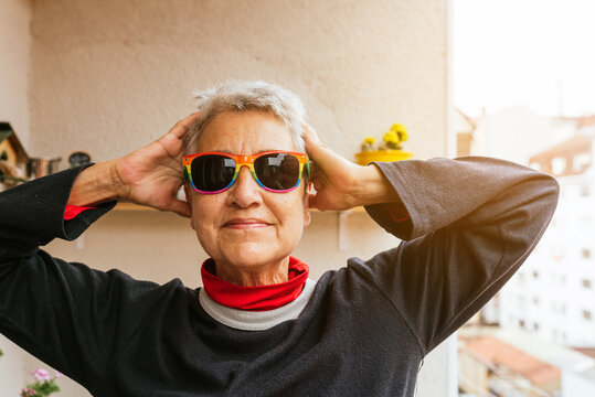 Vertical portrait of older lesbian woman with short gray hair wearing rainbow pride flag sunglasses smiling and touching her head. Human rights activist. lgbt community.
