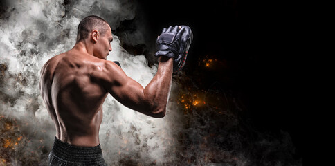 Muscular fighter posing with boxing paws against a background of smoke and fire. Mixed martial arts...