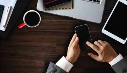 Cropped shot of male worker hands holding smartphone on dark modern office desk with office supplies