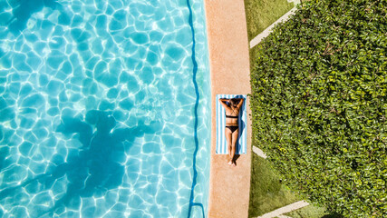 Fototapeta na wymiar A woman in bikini is resting on a towel by the hotel pool.