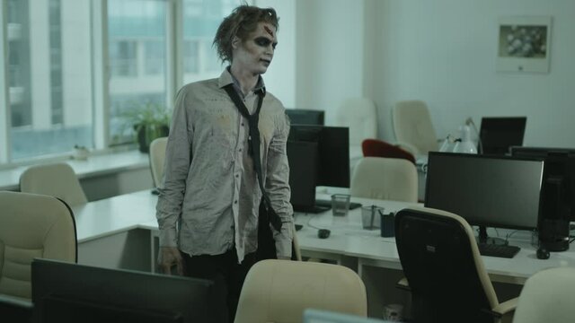 PAN shot of zombie businessman in torn shirt and necktie twitching and walking aimlessly in office