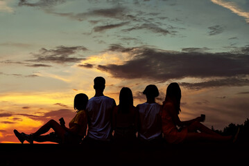 Silhouette of friends sitting on the curb and looking at the sky. Sunset and orange sky in the background. The concept of friendship and joy.