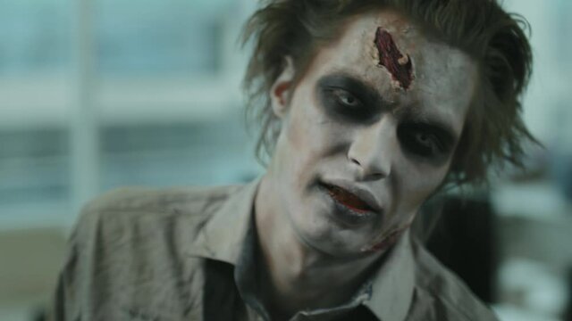Close up shot of brain-dead zombie man with SFX makeup and wounds twitching and looking around
