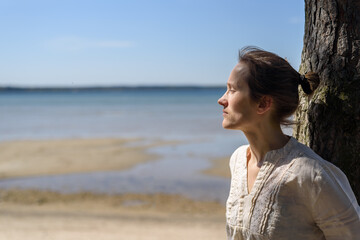 Woman in linen clothes standing near pine trees and looking to sea. Wellbeing, mental health