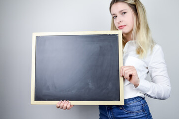 Portrait of a serious beautiful young blonde woman holding an empty chalkboard horizontally where you can add text, additional copy space over it	