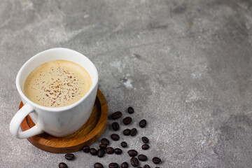 A Cup of hot Cappuccino coffee on wooden tray, with cofee beans on grey background. Selective focus, copy space.