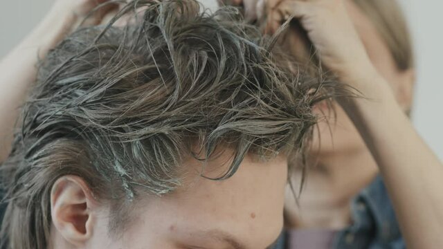 Tilt up close up of female hairstylist backcombing hair of male movie or stage actor