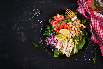 Buddha bowl dish with chicken fillet, chickpeas, tomatoes, red onion, fresh green salad and seed sesame. Healthy balanced eating. Top view, above, copy space
