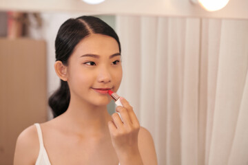 Beautiful young woman applying makeup near mirror in dressing room