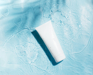 Cosmetic sunscreen product on blue water surface with splashes and drops. Body care health concept....