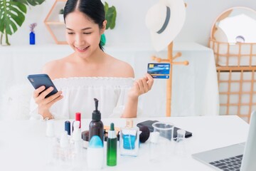 Asian beautiful woman using smartphone with credit card shopping online at home with cosmetic and skin care.Convenience in buying online products with modern business technology concept.