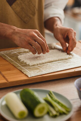 Close up making sushi. Male hands preparing rice for rolling on a bamboo mat. Asian food delivery promo
