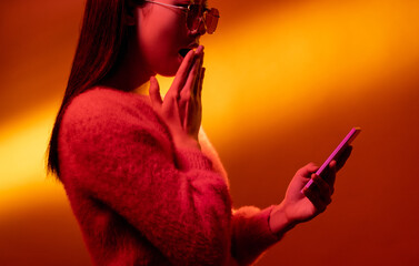Online surprise. Neon light people. Mobile application. Pink color profile portrait of amazed shocked Asian girl reading message with wow on phone on golden gradient copy space.