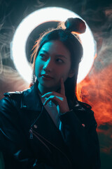 Cyberpunk people. Future mystery. Artificial intelligence. Blue neon light pensive curious Asian girl in black biker jacket with white circle halo in orange color fog at dark night.