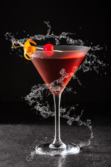 Traditional Manhattan cocktail with cherry splashing in glass on black background