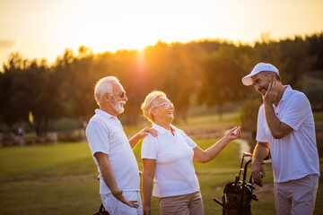 Three seniors golfers talking on golf field.  Golfer on the field sunset.