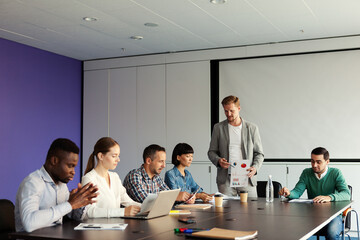 Group of diverse business people having meeting in conference room. Middle aged male manager presenting marketing report with data and graphs to collegaues sitting at table