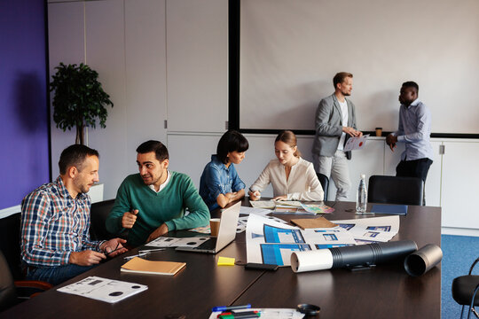 Team of  six diverse business people having meeting in conference room. Colleagues talking in pairs and discussing work at break in meeting