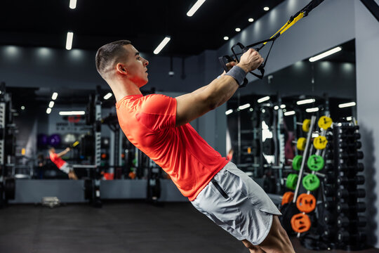 The man slowly and balanced performs exercises for the arms and the whole body on the fitness trx straps and holds the handles. Gym training, personal trainer