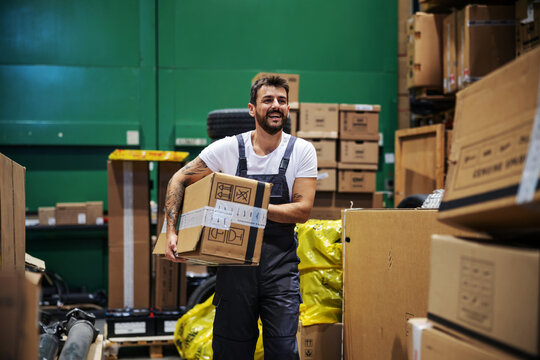 Hardworking Tattooed Bearded Manual Worker Walking Trough Warehouse And Carrying Very Heavy Big Box Ready For Export.