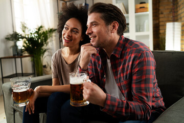 Boyfriend and girlfriend drinking beer at home. Happy couple watching sports game on tv..