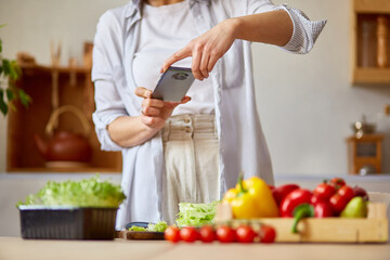 Woman taking photo of healthy salad with smartphone for her blog on kitchen at home
