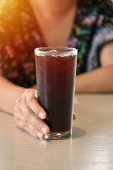 Vertical view, Iced coffee in tall glass with woman hand on wooden table.