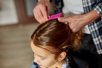 Father combing, brushing his daughter's hair at home