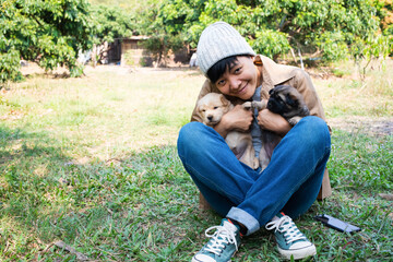 Smile Asian owner carrying, hugging adorable puppy dogs on her sitting green grass backyard lawn. Love pet concept