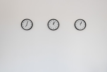 Three classic clocks hang isolated on light grey wall background.