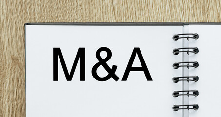 Notepad with text M and A on wooden deskt. Business and finance concept