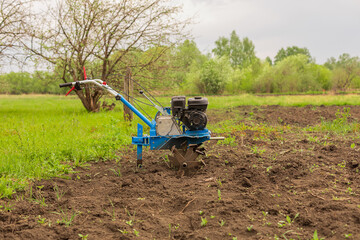 A blue walk-behind tractor stands on arable land. Agricultural vehicles cultivate the land. Arable...