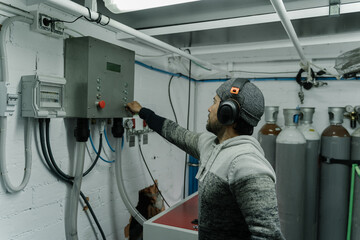 Man in cap and headphones using a control panel to refill gas cylinders inside a ship.