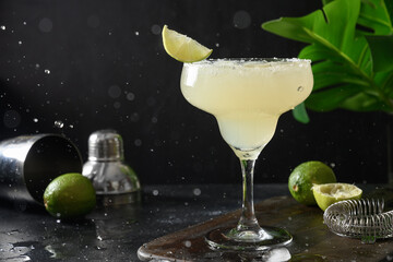 Classic Margarita or Daiquiri cocktail with lime juice and ice cube on dark black background with...