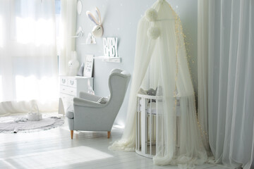 Stylish scandinavian interior of newborn baby room with bed and grey armchair. Hanging white canopy with cradle. Decor children room with furniture. Crib in a modern nursery room. Baby cot with canopy © stock_studio