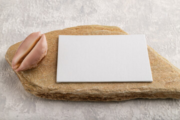 White paper business card, mockup with stone and seashell on gray concrete background. side view, copy space.