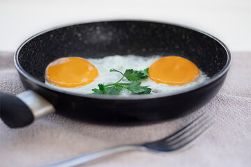 Side view of fried eggs with parsley in a frying pan closeup. Selective focus