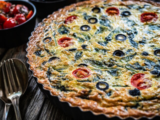 Millet quiche with spinach, black olives, cherry tomatoes and ricotta on wooden table 