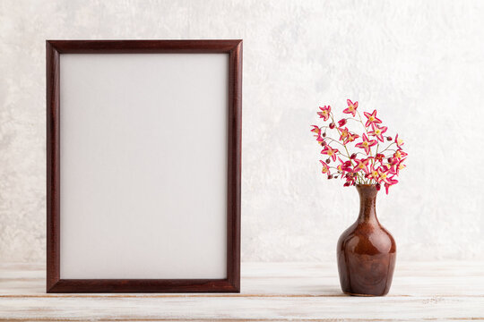 Wooden frame with purple barrenwort flowers in ceramic vase on gray concrete background. side view, copy space, mockup.