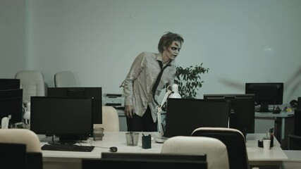 Handheld medium shot of businessman in suit holding baseball bat and trying to protect himself from zombie man in torn clothes in office, then running away