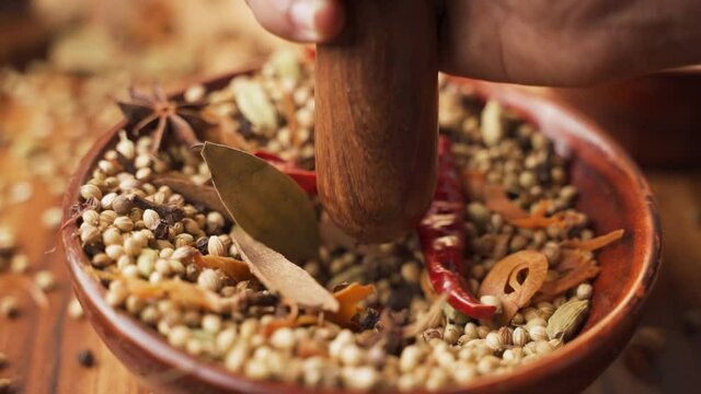 Close up of smashing Indian mixed Masala ingredients in the wooden bowl or Spice Grinder mortar for sambar spice - Concept of Preparation of Indian masala spices.