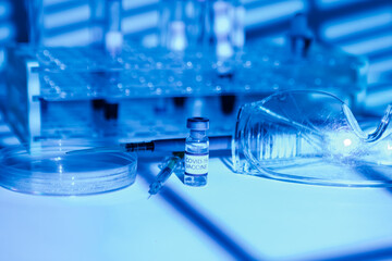Laboratory table with support for test tubes, vial with vaccine for COVID-19, syringe, pipette, protective glasses and petri dish, with blue light environment
