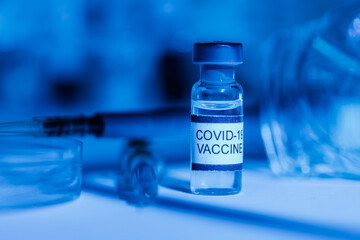 Laboratory table with support for test tubes, vial with vaccine for COVID-19, syringe, pipette, protective glasses and petri dish, with blue light environment