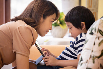 Asian woman is looking at boy using a tablet.