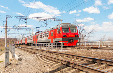 Fototapeta na wymiar An electric train runs on rusty railroad tracks against a blue sky with white clouds.