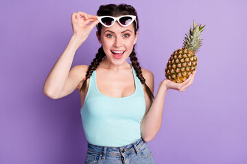 Portrait of attractive cheerful girl touching specs holding in hand juicy ananas isolated over violet purple color background